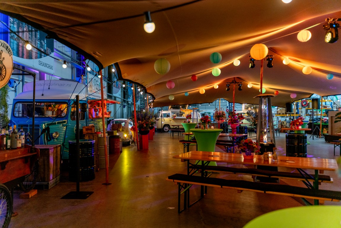 Sfeervol ingericht event met foodtrucks, verlichting en zitplekken in industriële hal
